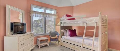 A bedroom with a bunk bed, a dresser, a chair, a small table, and a window with curtains.
