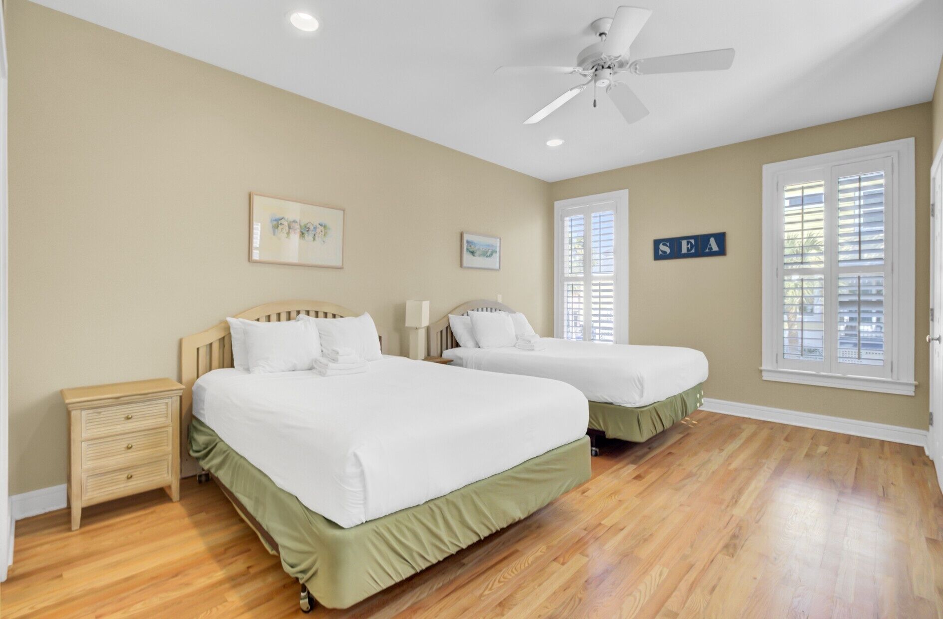 A bedroom with two beds, a nightstand, a ceiling fan, and a window with blinds.