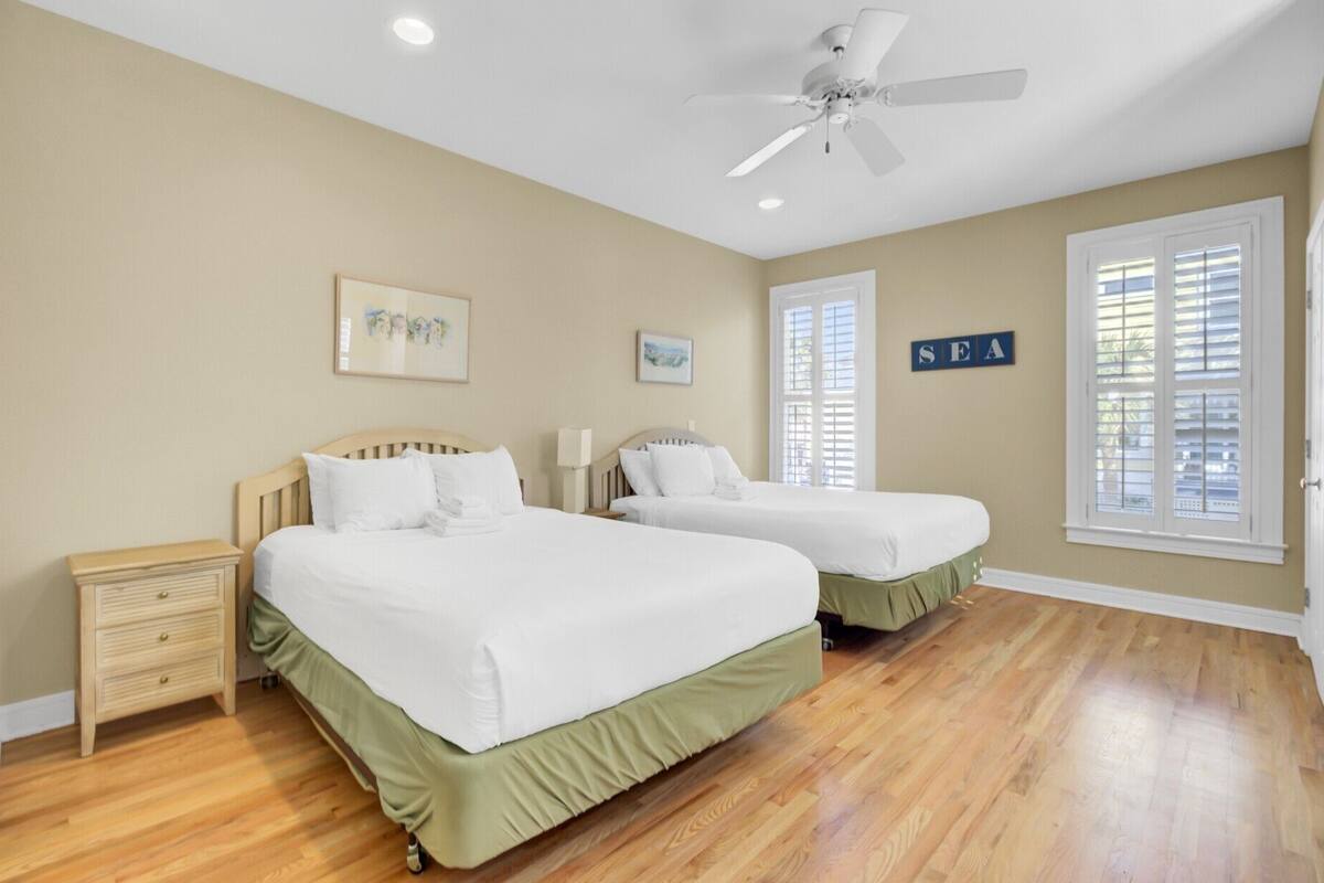 A hotel room with two beds, a ceiling fan, and a window with blinds.