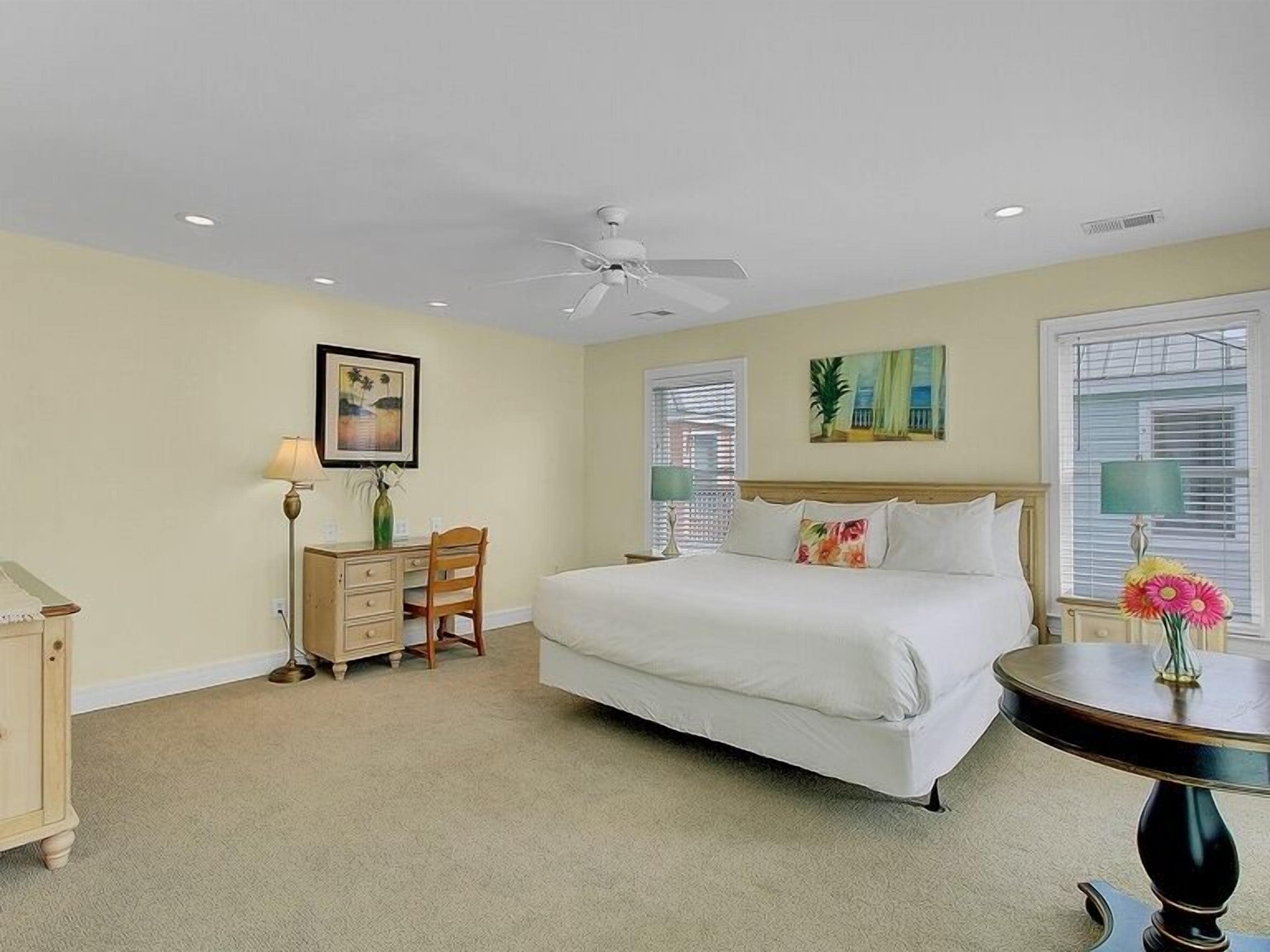 A bedroom with a bed, a desk, a chair, a round table, and a ceiling fan.