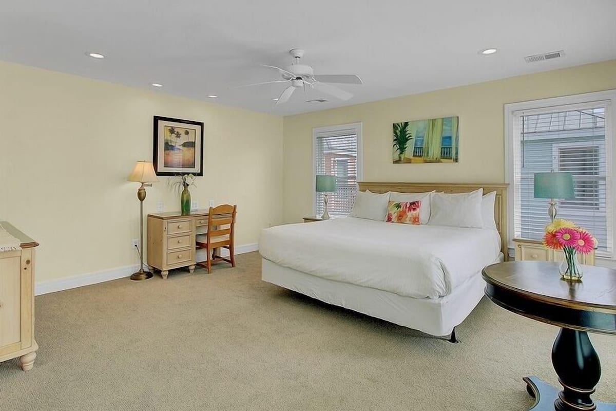 A bedroom with a bed, a desk, a chair, a round table, and a ceiling fan.