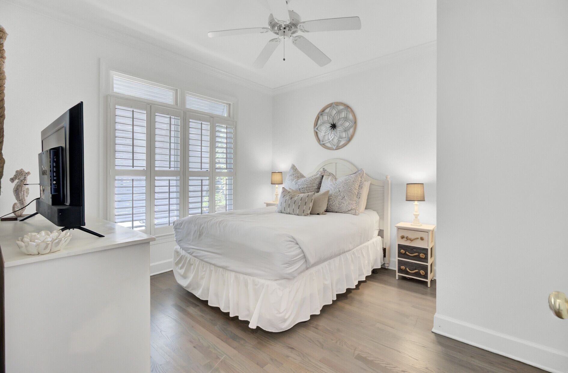 A bedroom with a bed, a ceiling fan, a TV, and a window with blinds.