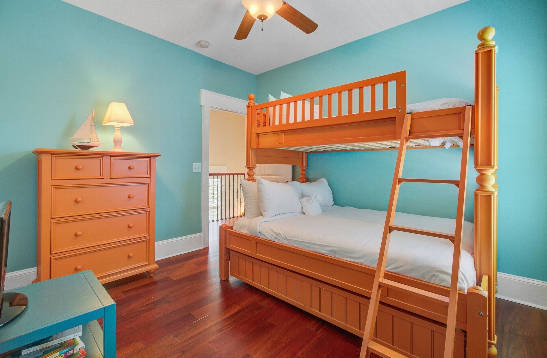 Une chambre avec un lit superposé, une commode, une lampe et un ventilateur de plafond.