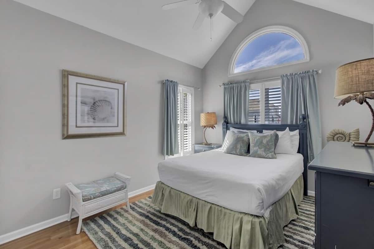 A bedroom with a bed, a bench, a desk, a lamp, and a framed picture on the wall.