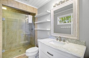 A bathroom with a glass-enclosed shower, a white toilet, a marble sink, and a mirror with a small window view. - Wild Dunes Vaction Homes 3&4 Bedrooms (Isle of Palms)
