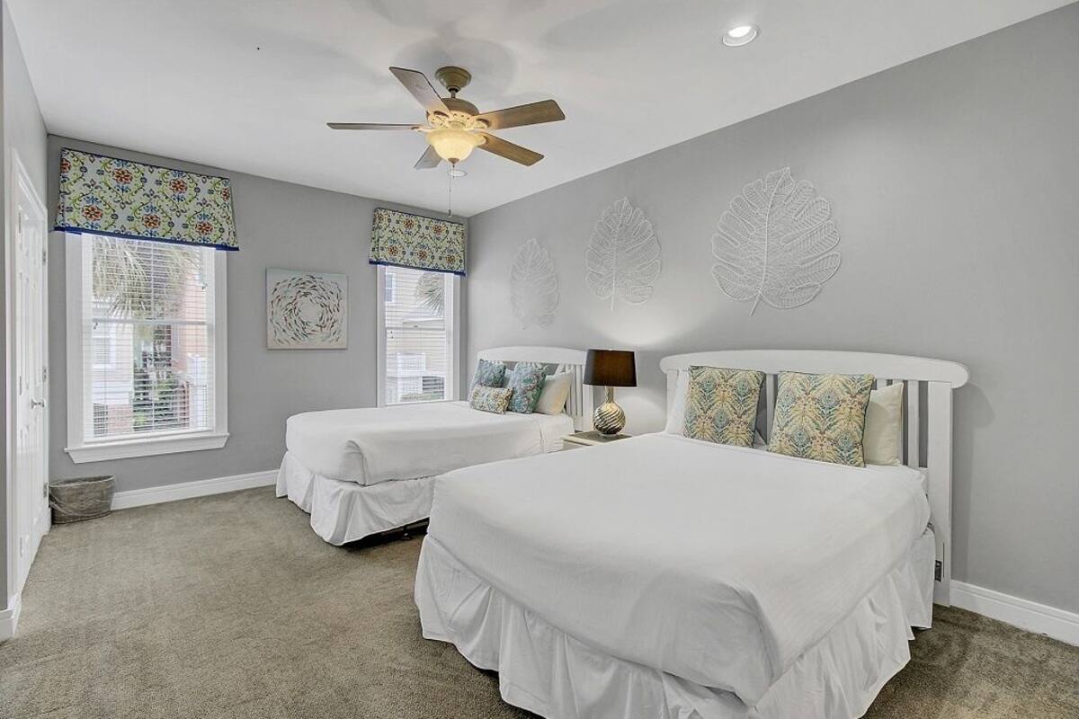 A bedroom with two beds, a ceiling fan, and leaf-patterned wall art.