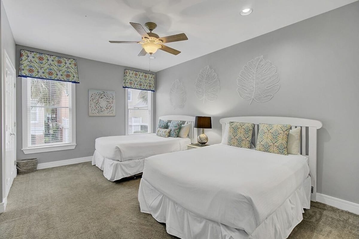 A bedroom with two beds, a ceiling fan, and leaf-patterned wall art.