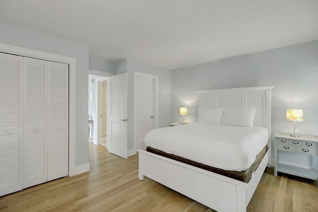A bedroom with a bed, nightstands, a wardrobe, and a door leading to another room.