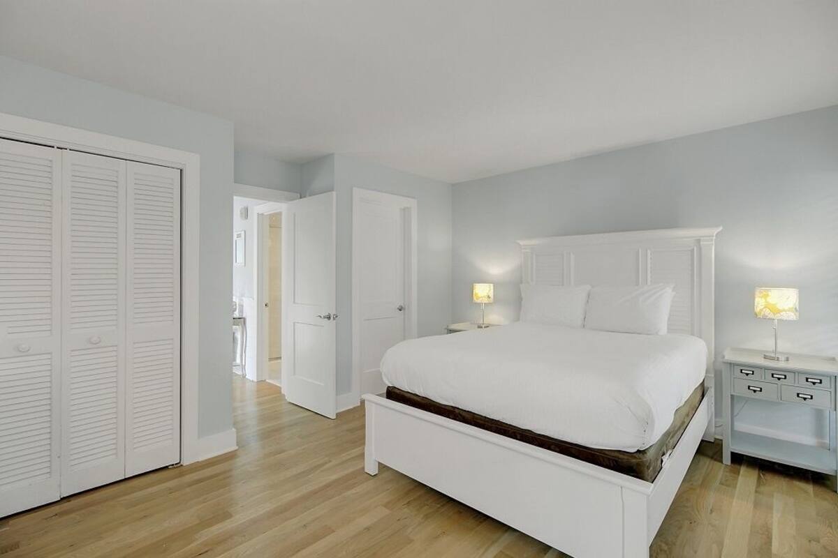 A bedroom with a white bed, white nightstands, and a white wardrobe.