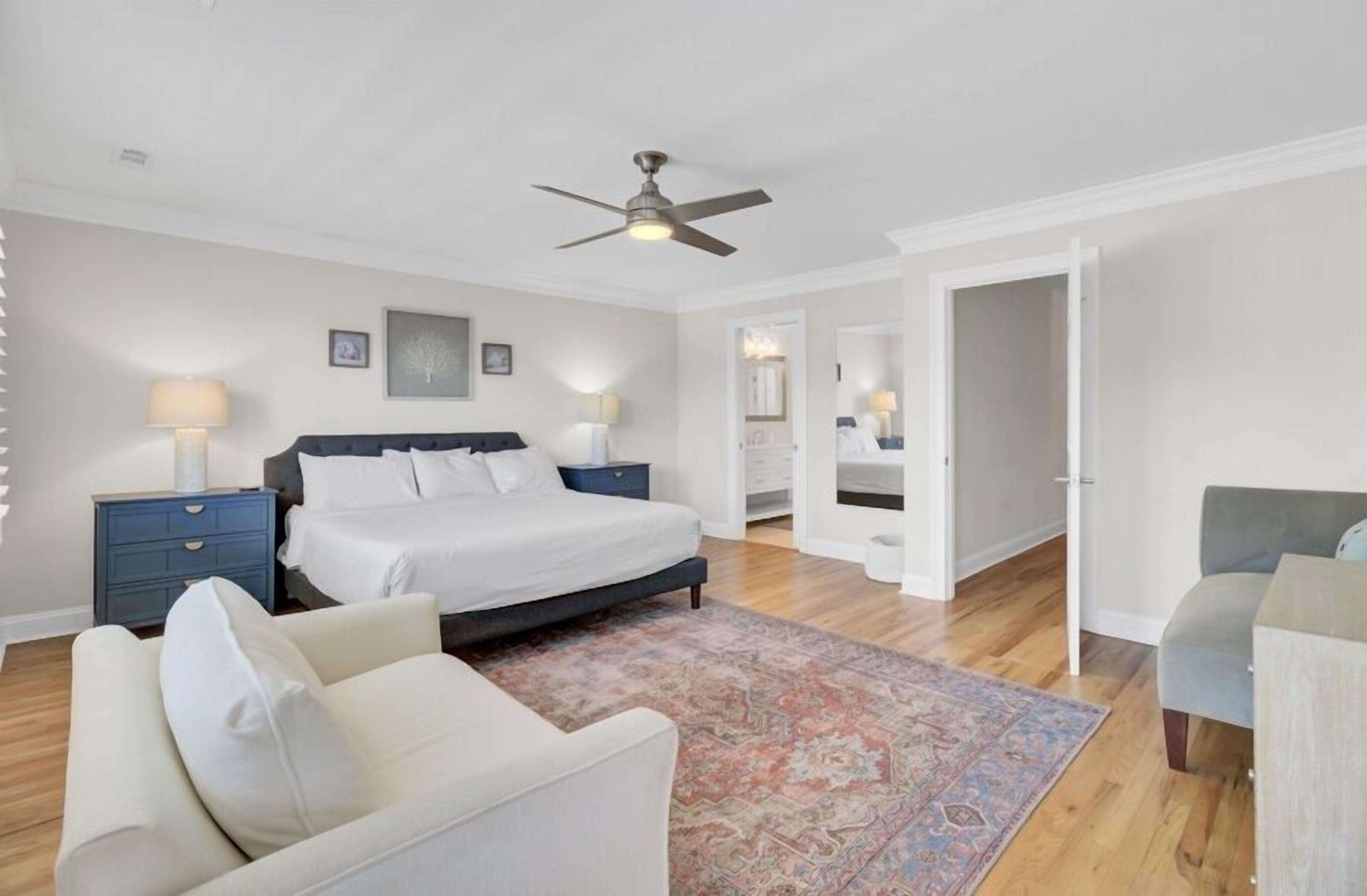 A bedroom with a bed, nightstands, a ceiling fan, a large rug, and a chair.