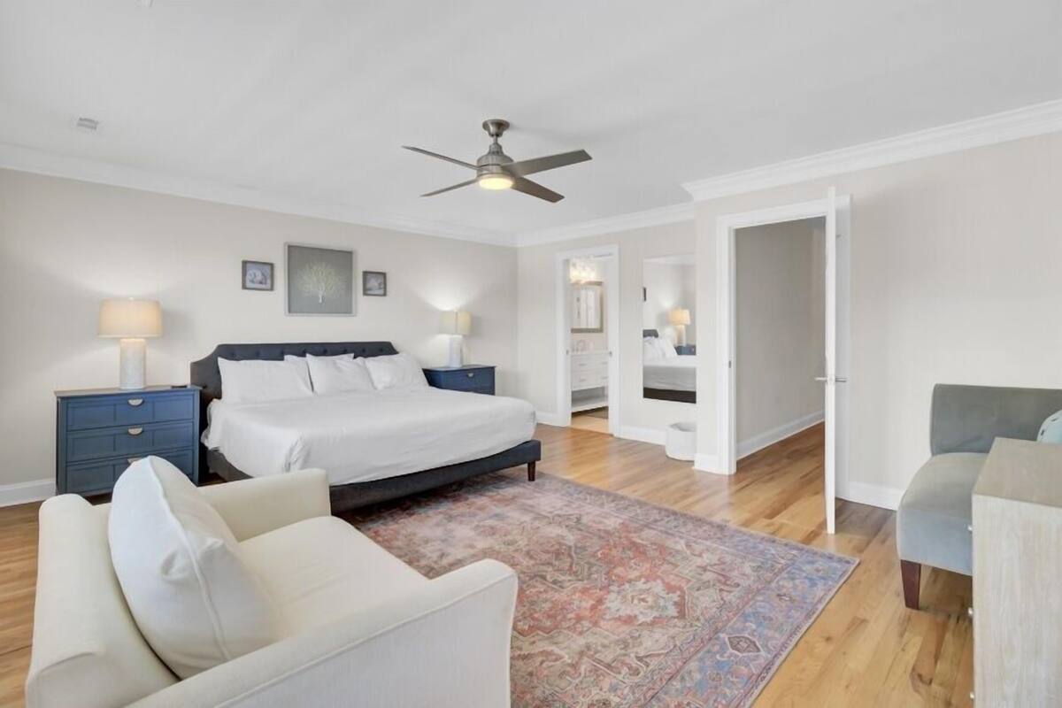 A bedroom with a bed, nightstands, a ceiling fan, a large rug, and a chair.