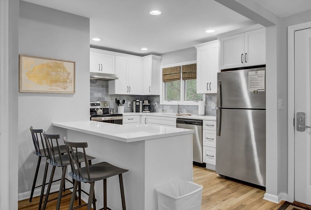 A modern kitchen with white cabinets, stainless steel appliances, and a bar area with stools.