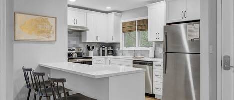 A modern kitchen with white cabinets, stainless steel appliances, and a bar area with stools.