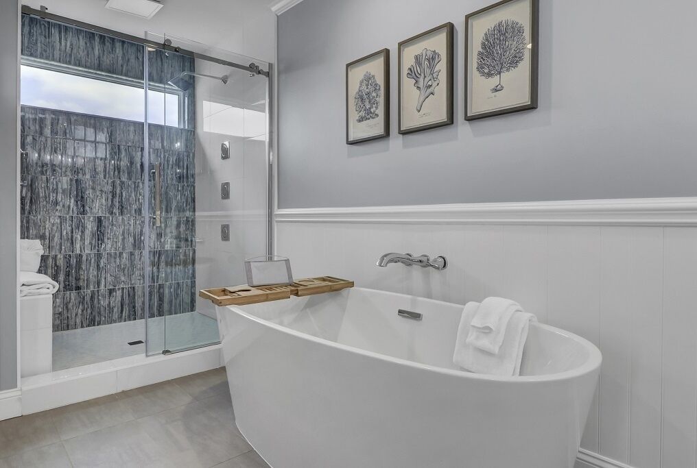 A bathroom with a freestanding bathtub, a glass shower enclosure, and three framed botanical prints on the wall.