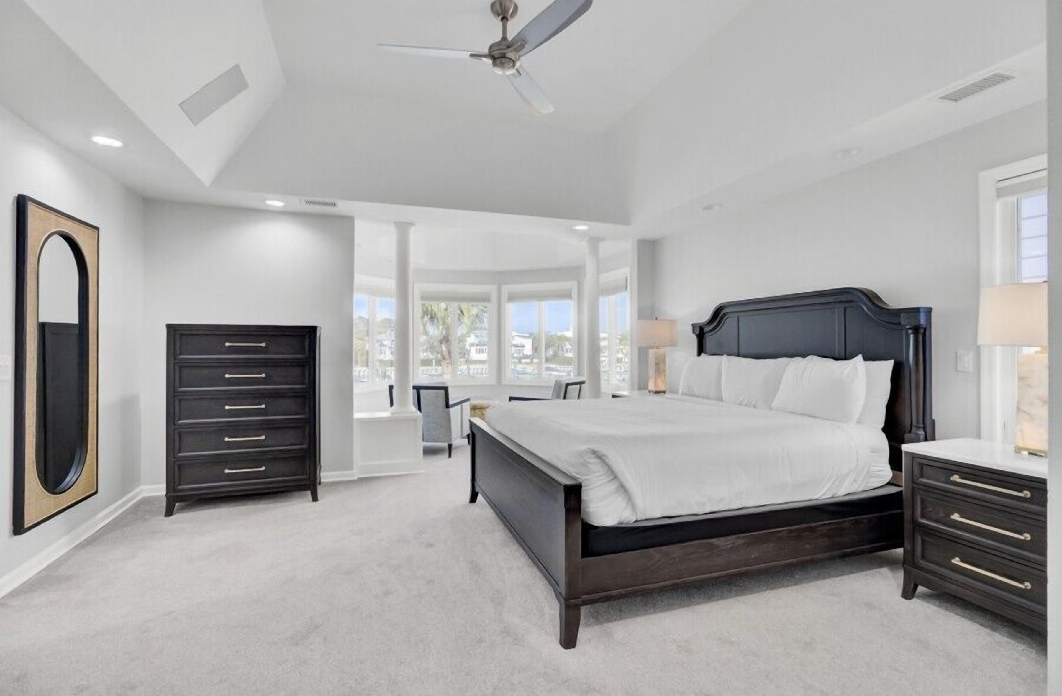 Ein Schlafzimmer mit einem großen Bett, einem Schminktisch, einem Spiegel und einem Deckenventilator.