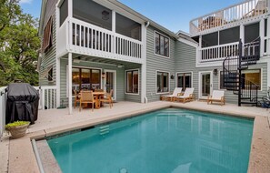 Ein zweistöckiges Haus mit Schwimmbecken, Außenmöbeln und einer überdachten Terrasse.