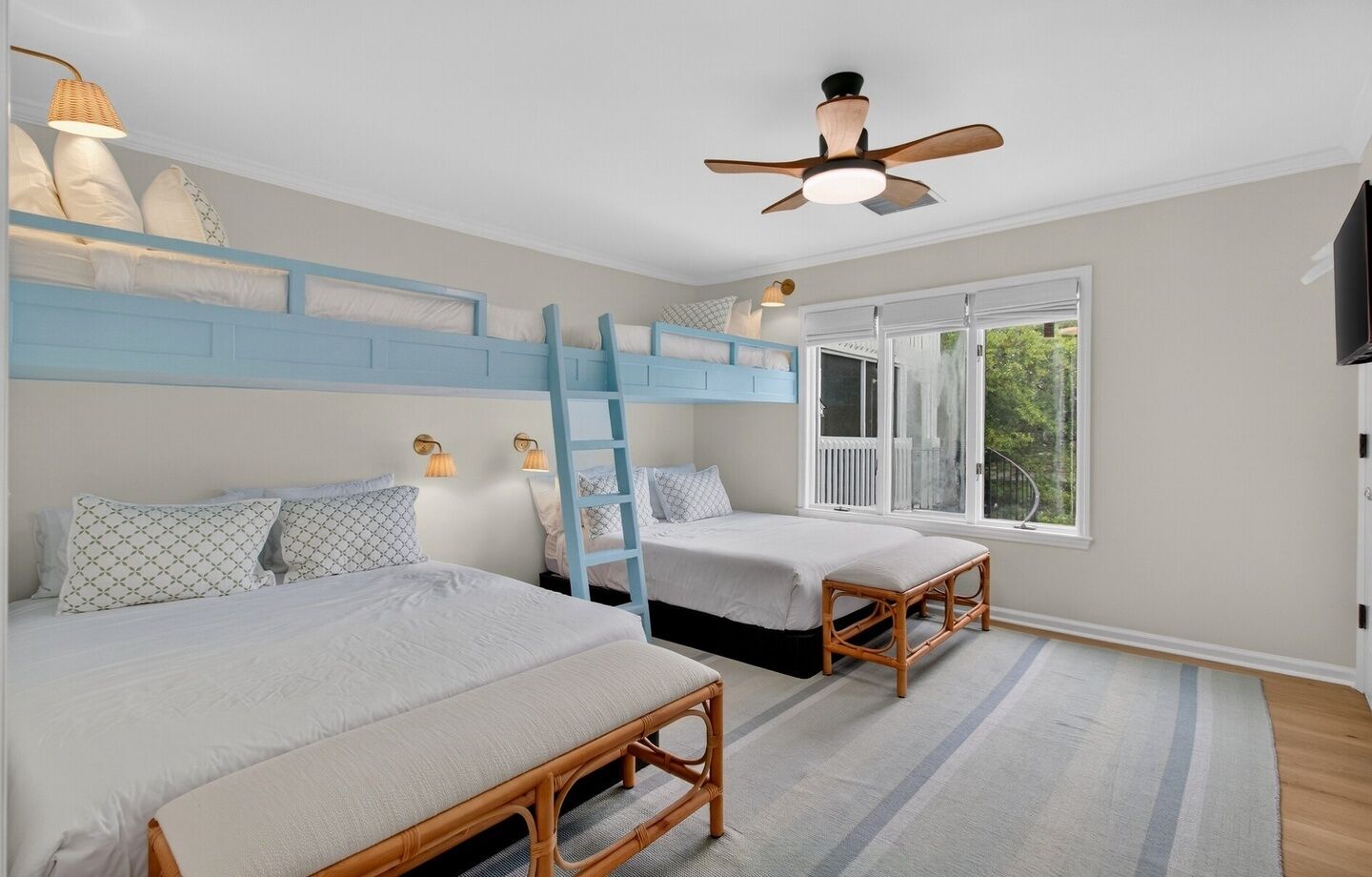 Ein Schlafzimmer mit Etagenbetten, einem Deckenventilator, einem Fenster mit Blick und einer Holzbank.