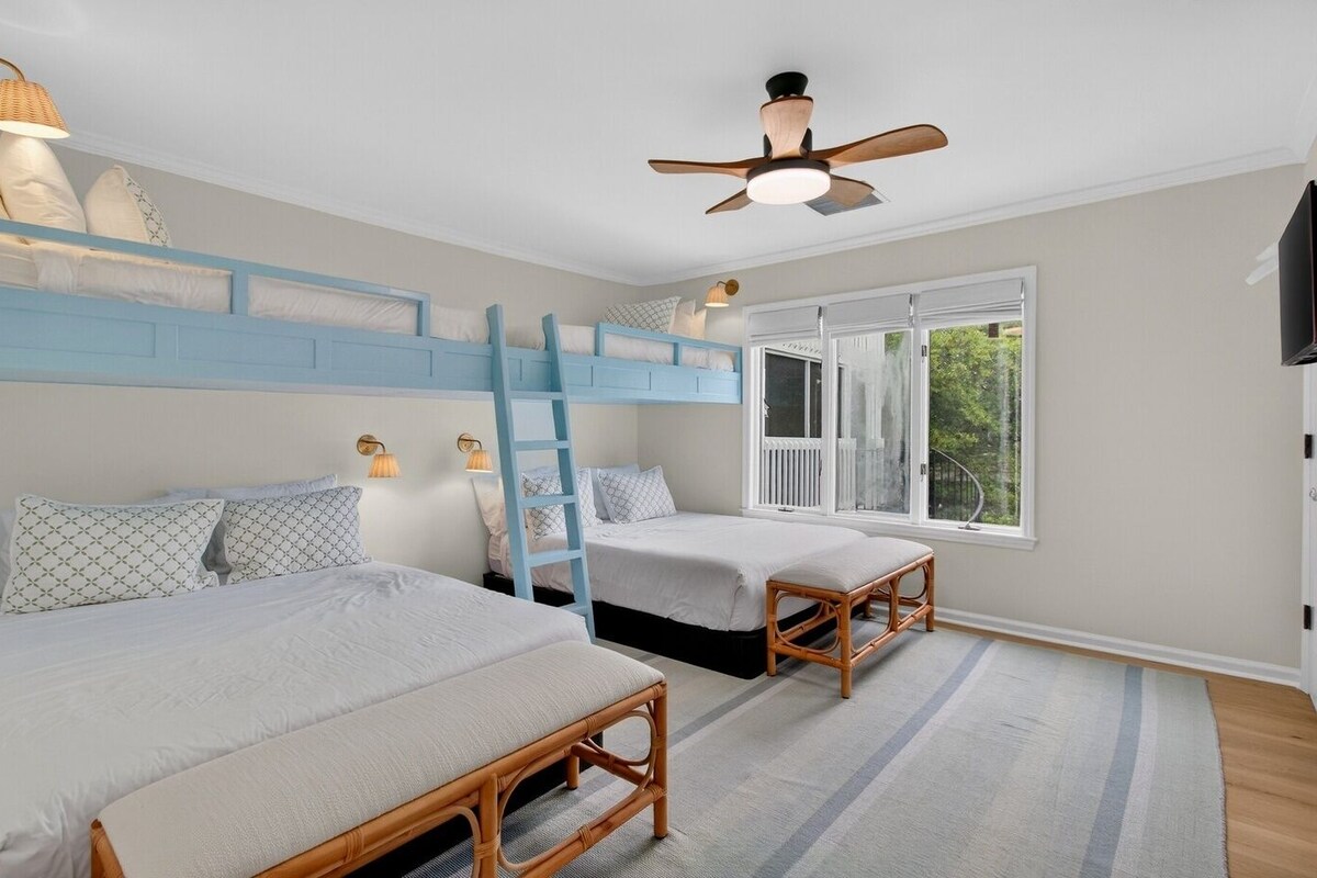 Ein Schlafzimmer mit Etagenbetten, einem Deckenventilator, einem Fenster mit Blick und einer Holzbank.