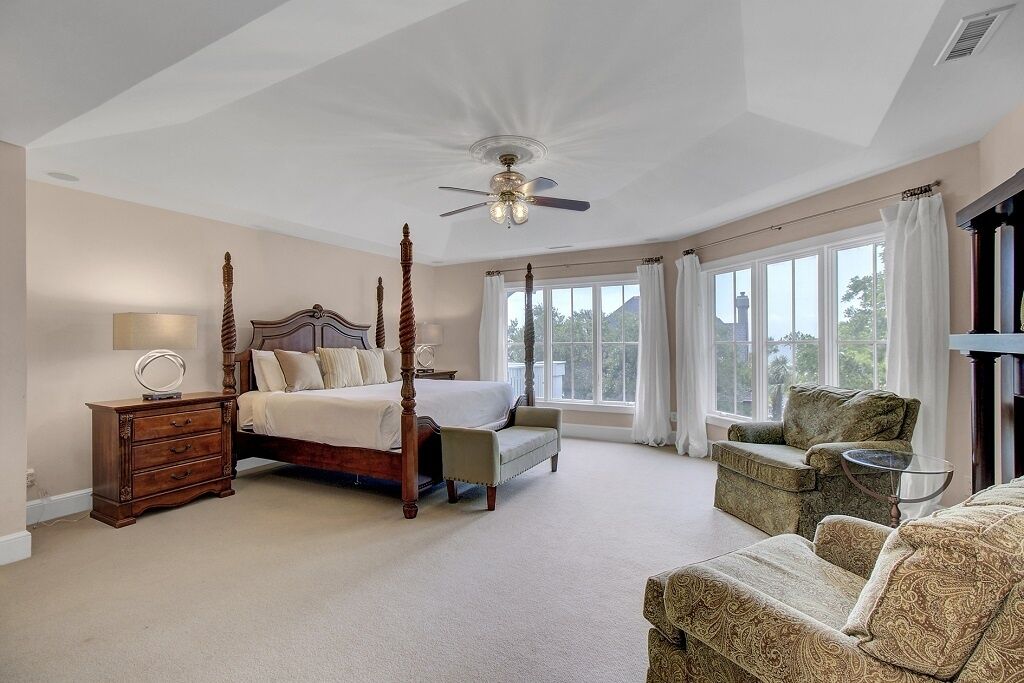 Ein geräumiges Schlafzimmer mit einem Himmelbett, einer Sitzecke mit Sofa und Sessel, und großen Fenstern mit Blick ins Freie.
