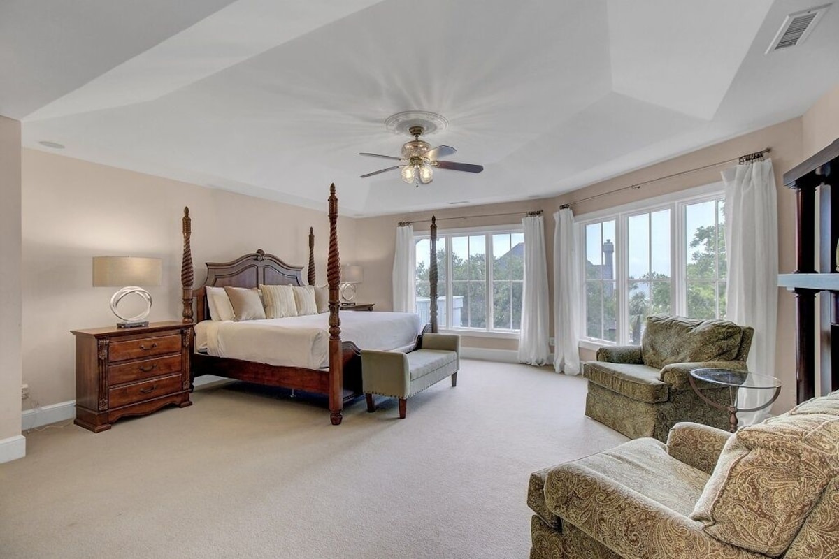 Ein geräumiges Schlafzimmer mit einem Himmelbett, einer Sitzecke mit Sofa und Sessel, und großen Fenstern mit Blick ins Freie.