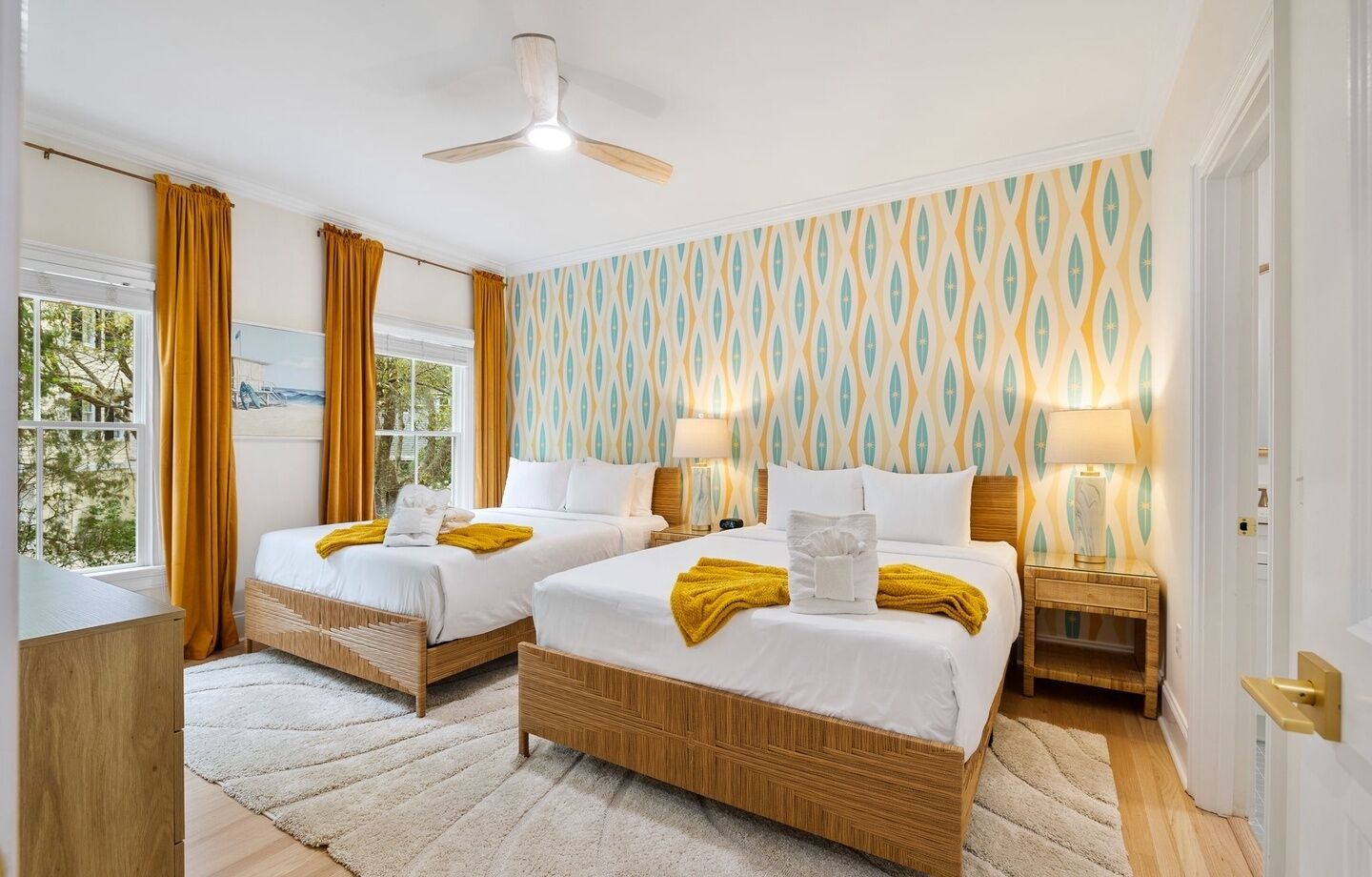 Ein Hotelzimmer mit zwei Betten, einem Deckenventilator, einem Fenster mit Vorhängen und einer Wand mit Muster.