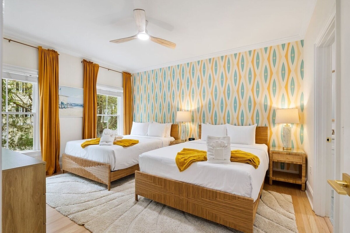 Ein Hotelzimmer mit zwei Betten, einem Deckenventilator, einem Fenster mit Vorhängen und einer Wand mit Muster.