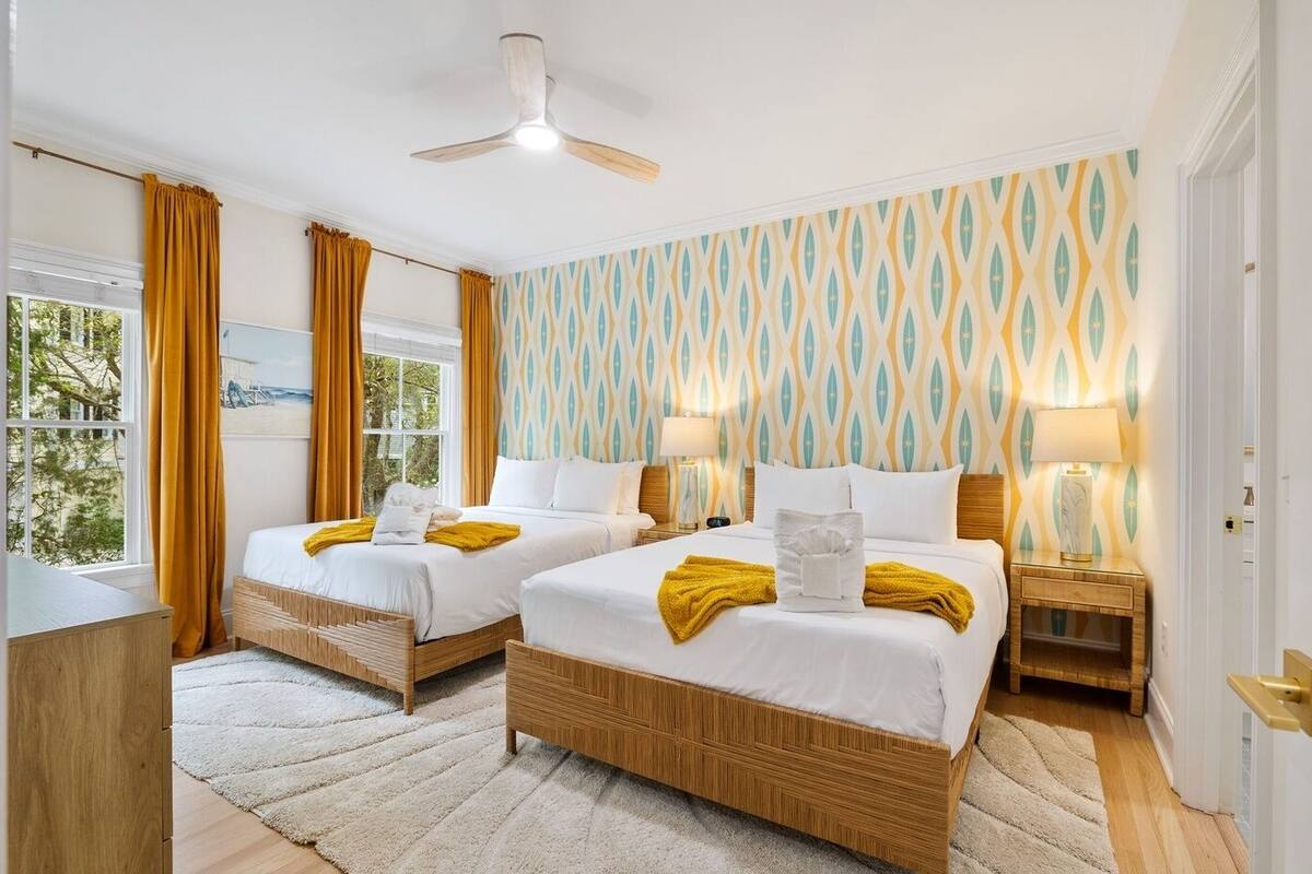 Ein Hotelzimmer mit zwei Betten, einem Deckenventilator, einem Fenster mit Vorhängen und einer Wand mit Muster.