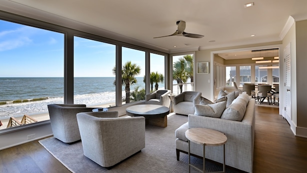 Ein geräumiger Wohnbereich mit großen Fenstern und Blick auf einen Strand, ausgestattet mit modernen Sofas und einem Couchtisch.