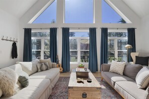 A spacious living room with a high ceiling, large windows, a sofa, a coffee table, and a guitar. - The Rail & Pine Spacious Masthope Mountain Retreat (Lackawaxen)