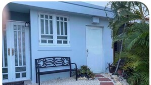 A house with a white door, a bench, and a garden with gravel and plants. - Private Mini Villa w/ Pool, Terrace, BBQ & Secure Parking in Ponce (Ponce)