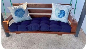 A wooden swing bench with a dark blue cushion and two decorative pillows with shell designs. - Private Mini Villa w/ Pool, Terrace, BBQ & Secure Parking in Ponce (Ponce)