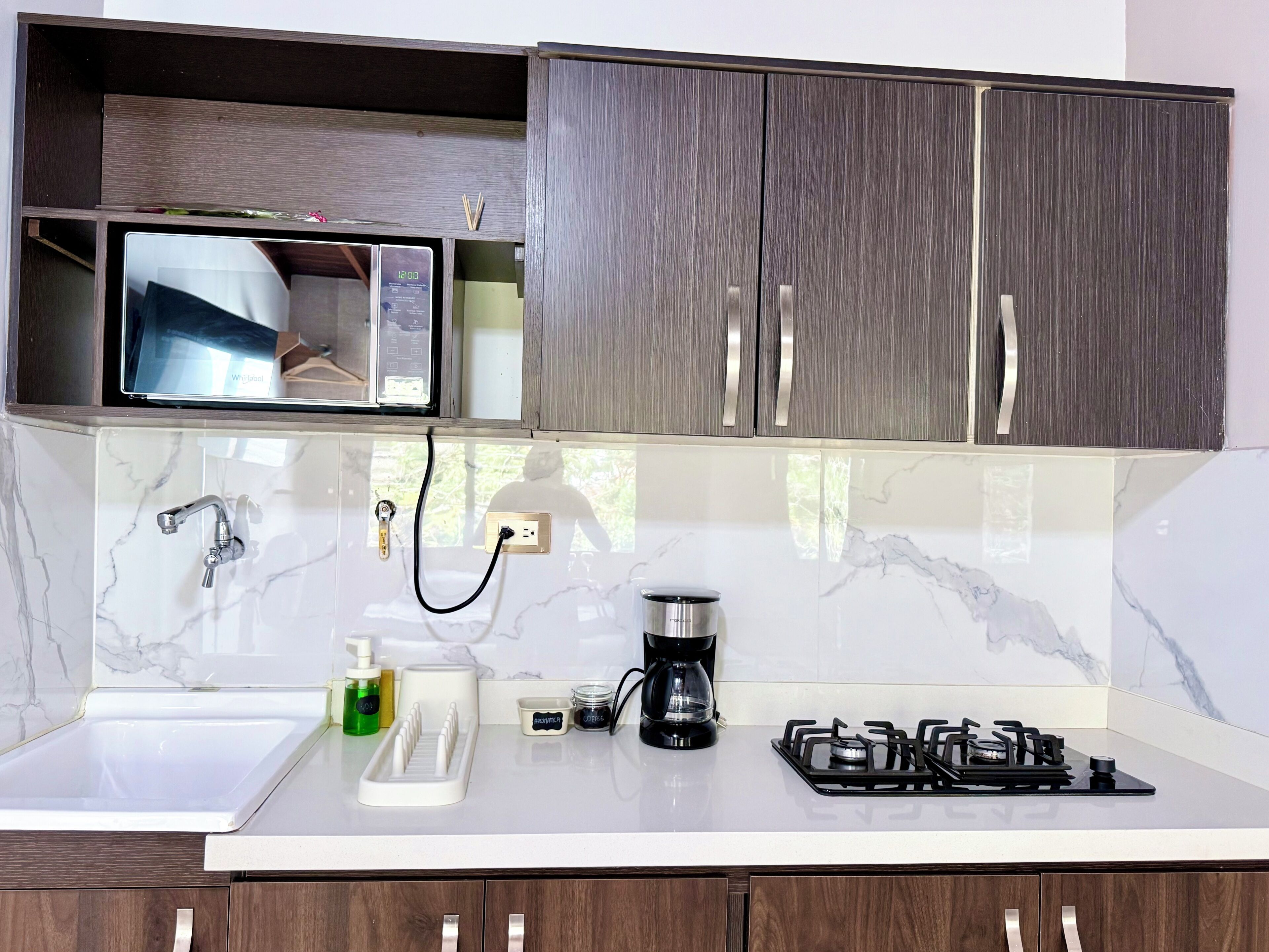 Una cocina moderna con microondas integrado, cafetera, estufa a gas y lavamanos con grifo.