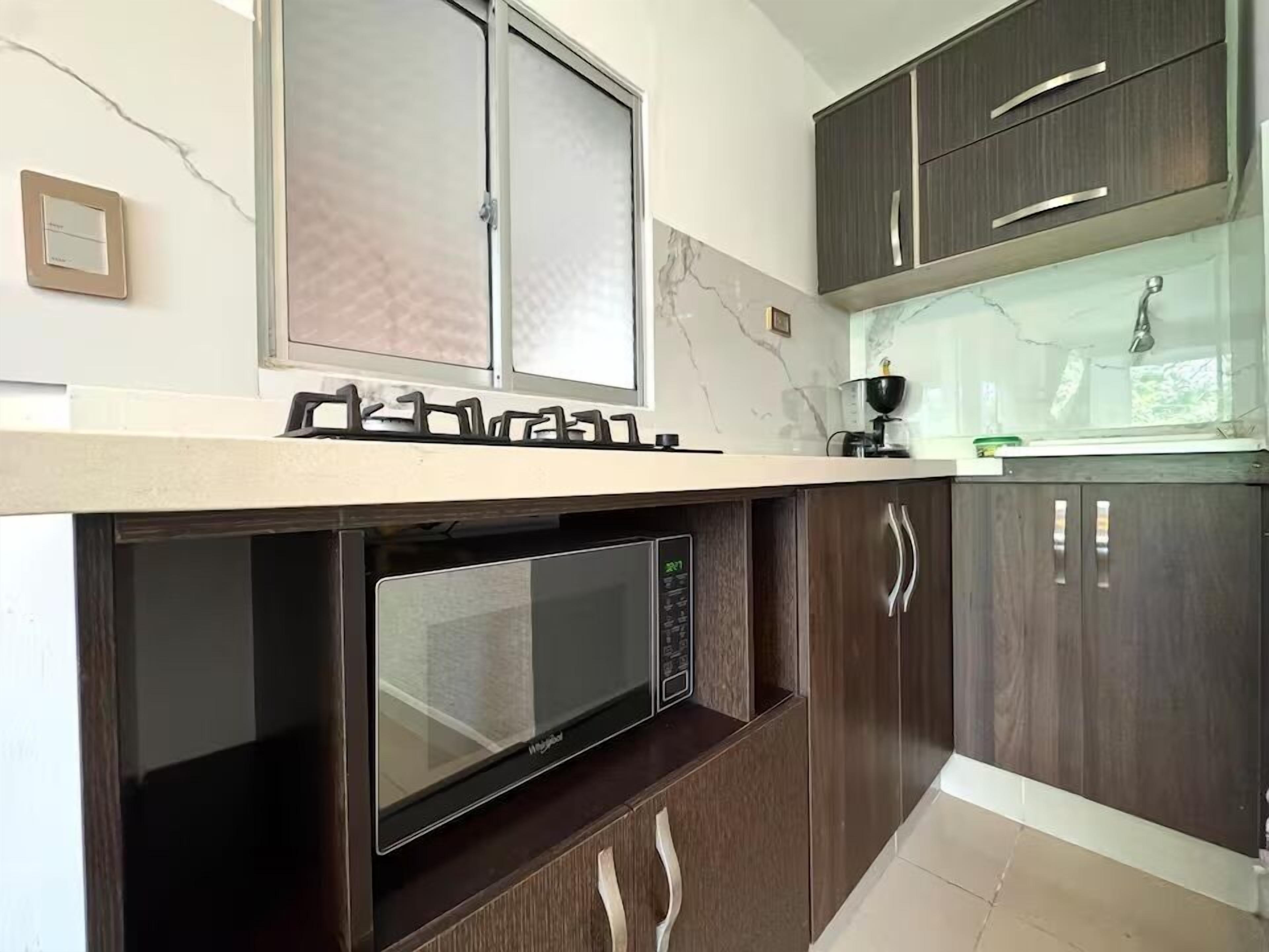 A kitchen with a built-in microwave, dark wooden cabinets, a marble backsplash, and a window with a frosted glass door.