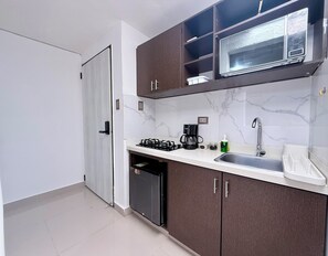 Una cocina compacta con estufa a gas, cafetera, microondas y pileta.