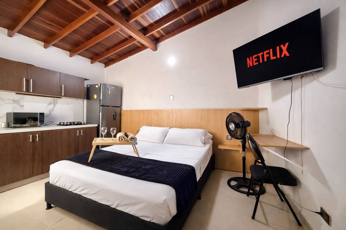 A hotel room with a bed, a TV mounted on the wall, a microwave, a refrigerator, and a wooden ceiling.
