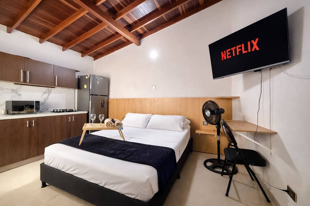 A hotel room with a bed, a TV mounted on the wall, a microwave, a refrigerator, and a wooden ceiling.