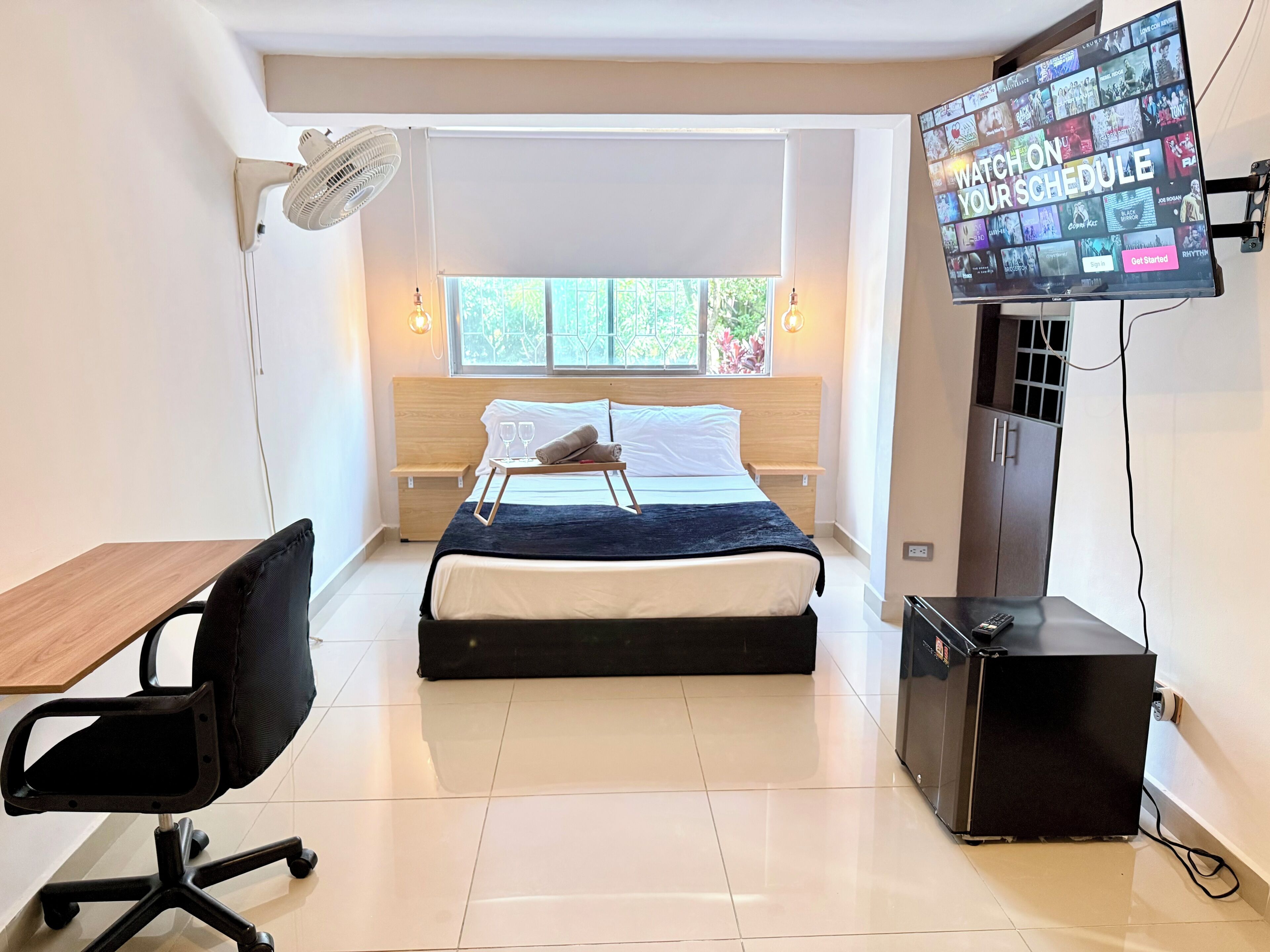 A modern bedroom with a bed, bedside table, chair, TV, and a desk.