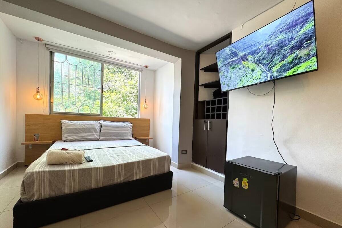 A bedroom with a bed, a television mounted on the wall, and a small black cabinet.