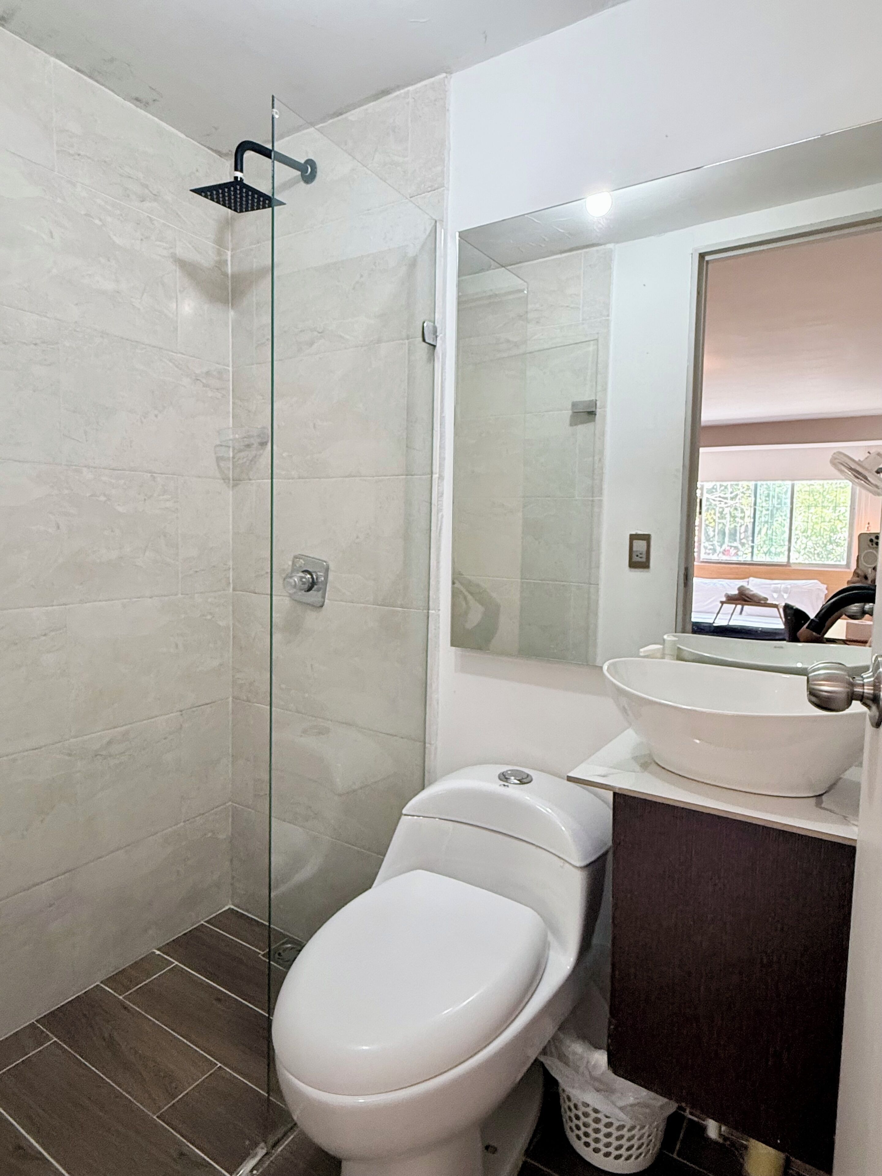 A bathroom with a glass-enclosed shower, a white toilet, and a sink with a mirror above it.