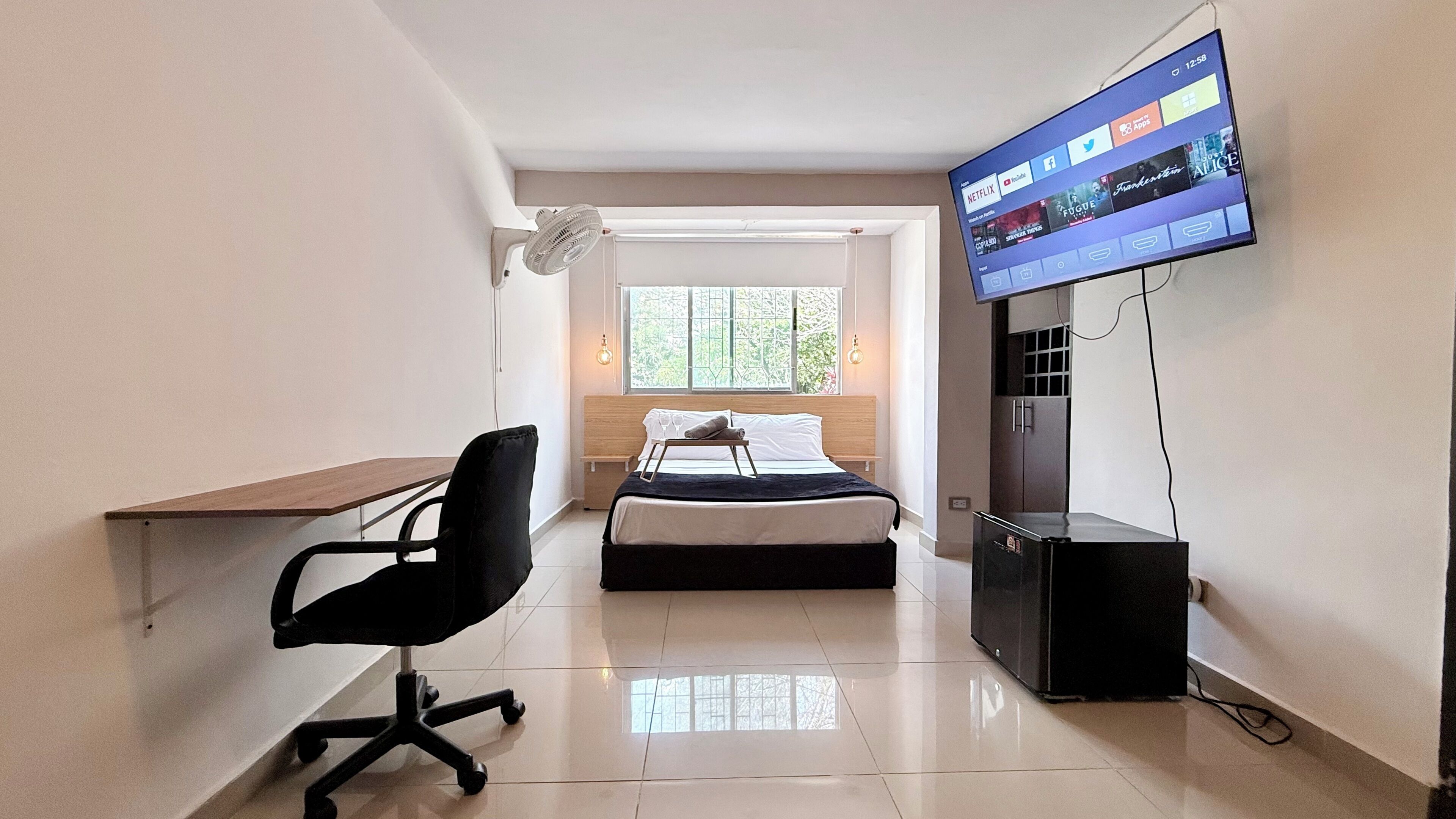 A compact hotel room with a bed, a desk, a chair, a TV, and a window.