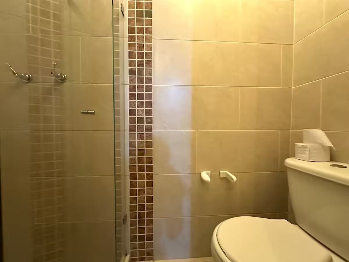 A bathroom with a glass shower enclosure, a toilet, and a tiled wall.