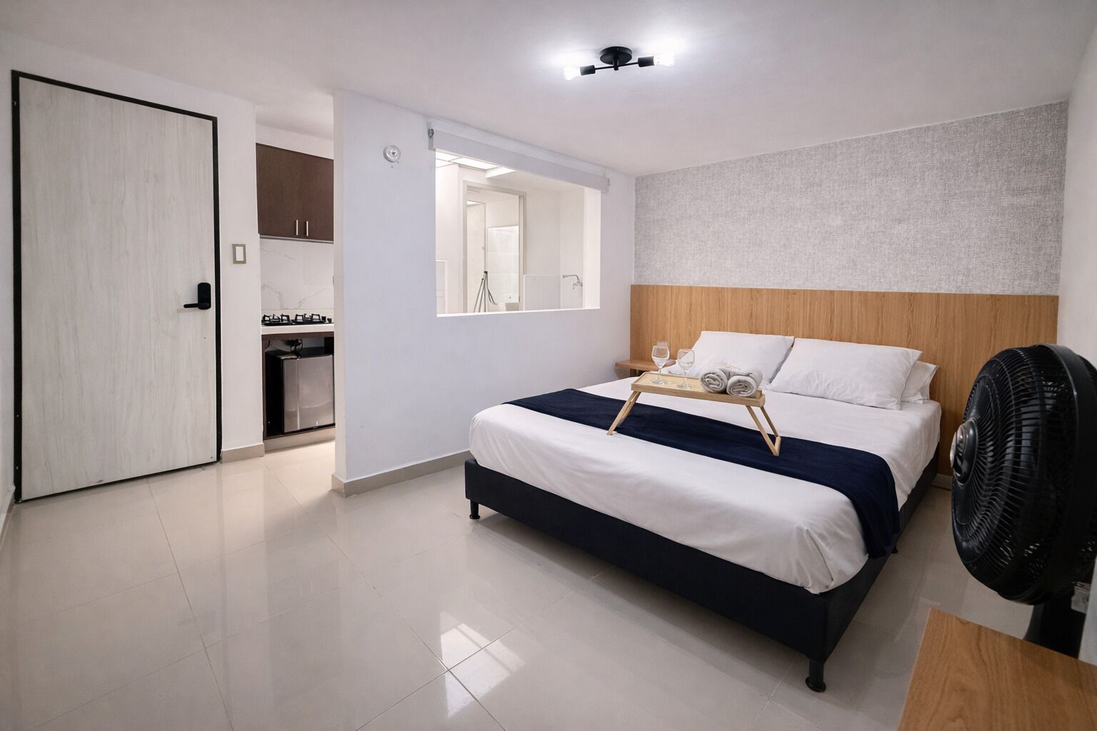 A modern hotel room with a bed, bedside table, and a fan.