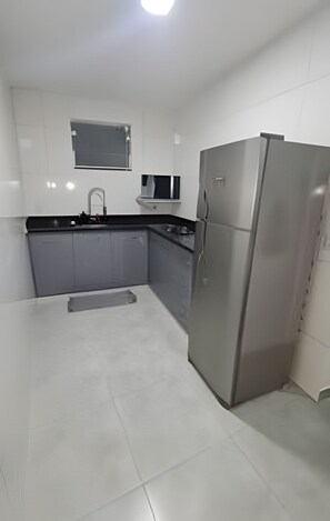 Uma cozinha com geladeira de aço inoxidável, armários cinzas, bancada preta e janela sobre a pia.