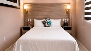 A hotel room with a large bed, two bedside tables with lamps, a wall-mounted phone, and a small shelf with bottles. - Standard plus room 207 9 minutes from Val'Quirico (Tetlatlahuca)