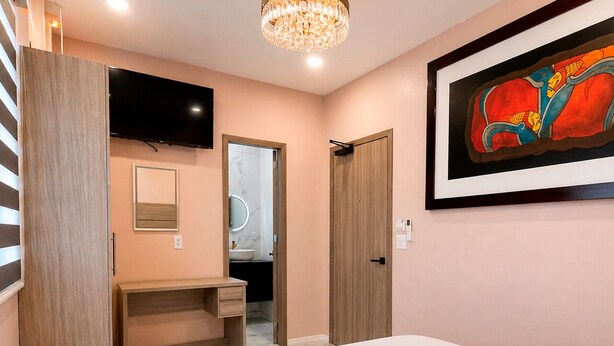 A bedroom with a bed, a TV mounted on the wall, a desk, and a door leading to a bathroom. - Standard plus room 207 9 minutes from Val'Quirico (Tetlatlahuca)