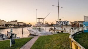 A marina with a docked boat, a pedestrian walkway, and a row of houses in the background. - Padre Island Resting Beach Face Studio Indoor Outdoor Pool Fish Docks Boat Slips (Corpus Christi)