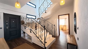 Un escalier orné de rampes noires, une porte sombre et une vue sur un coin cuisine.