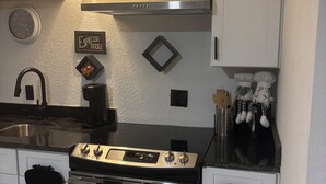 Une cuisine avec des meubles blancs, une cuisinière en acier inoxydable, une horloge et un luminaire fixé au mur.