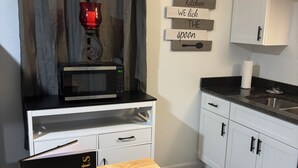 Une cuisine moderne équipée d’un four à micro-ondes, d’une table en bois avec une inscription, de meubles blancs et d’un rideau.