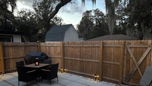 Une terrasse avec une table et des chaises, un barbecue et une clôture en bois.
